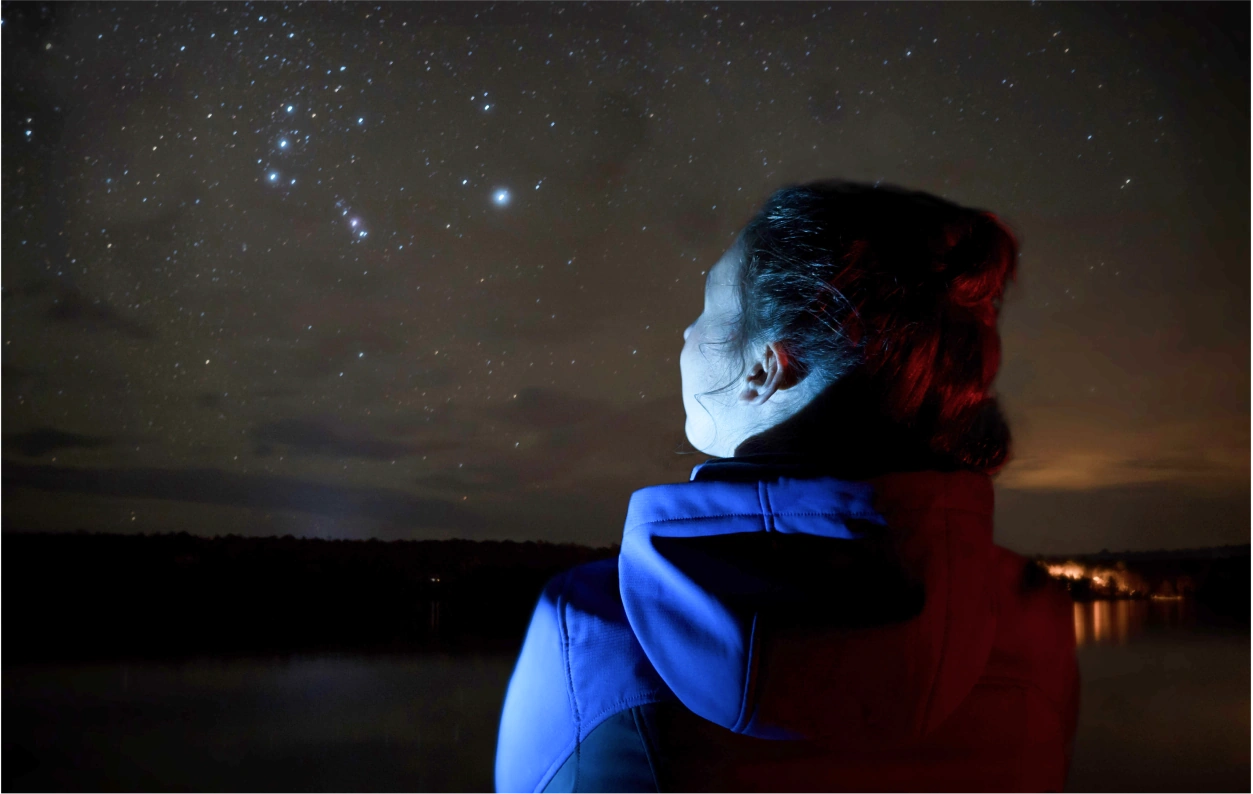 A person in a purple jacket looking up at the stars at night.
